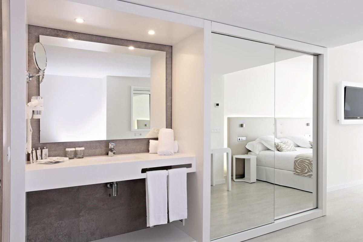 http://Salle%20de%20bain%20moderne%20blanche%20avec%20grand%20miroir%20et%20vue%20sur%20lit%20double%20de%20l'hôtel%20Iberostar%20Cala%20Millor%20à%20Majorque