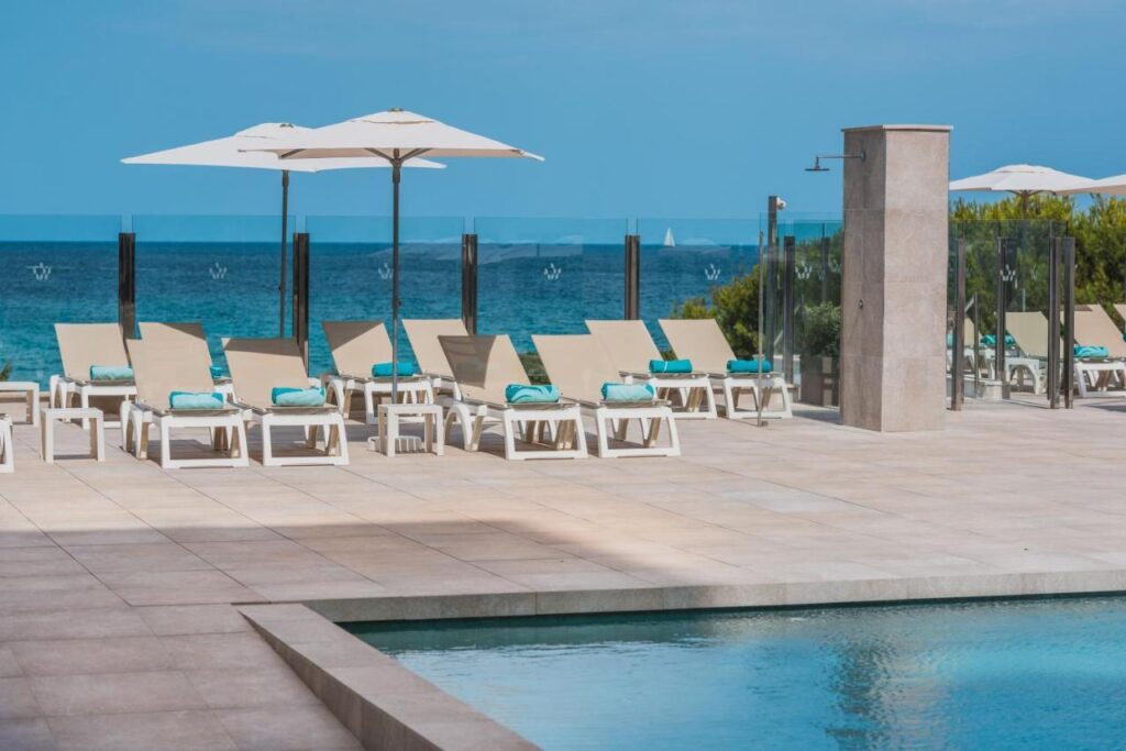 Chaises longues sur la terrasse de la piscine avec parasols et vue sur la mer à l'Iberostar Cala Millor
