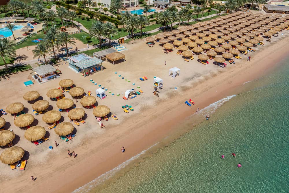 http://Vue%20aérienne%20d’une%20plage%20d’hôtel%20avec%20rangées%20de%20parasols%20en%20chaume%20et%20chaises%20longues
