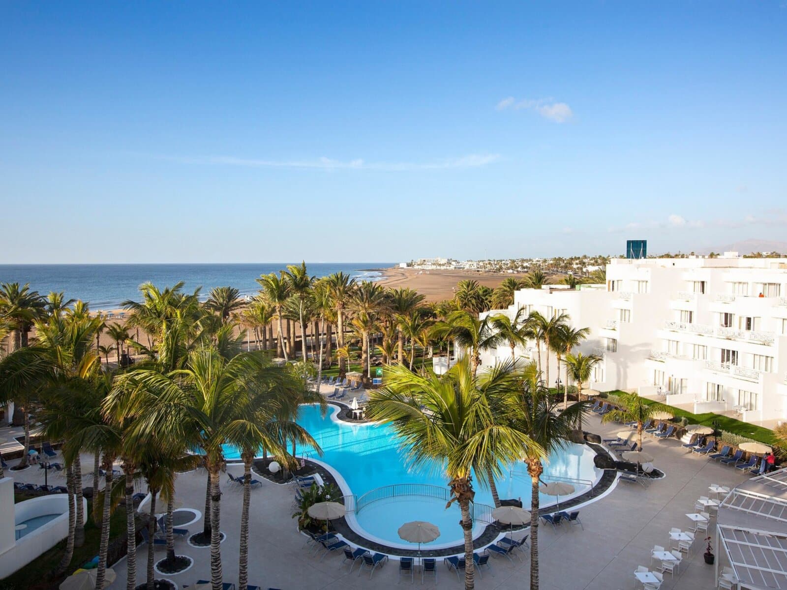 http://Vue%20aérienne%20d’un%20hôtel%20avec%20piscine,%20palmiers%20et%20plage%20en%20arrière-plan%20face%20à%20l’océan.