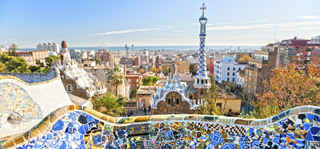 Vue depuis le parc Güell à Barcelone avec ses mosaïques colorées en premier plan et la ville s'étendant jusqu'à la mer Méditerranée en arrière-plan.