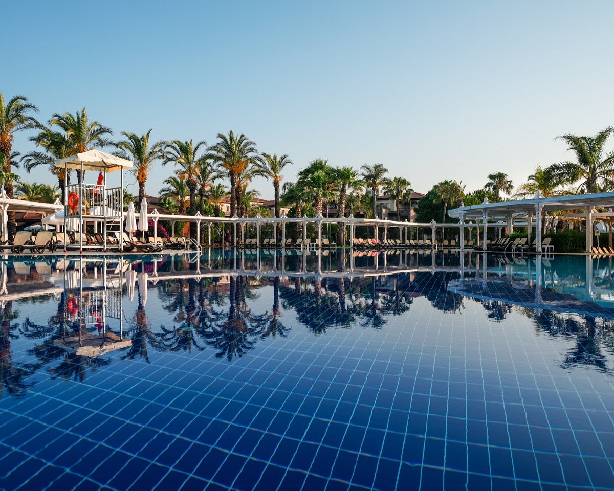 http://Grande%20piscine%20extérieure%20avec%20transats,%20palmiers%20et%20pergolas%20dans%20un%20hôtel%20de%20luxe.