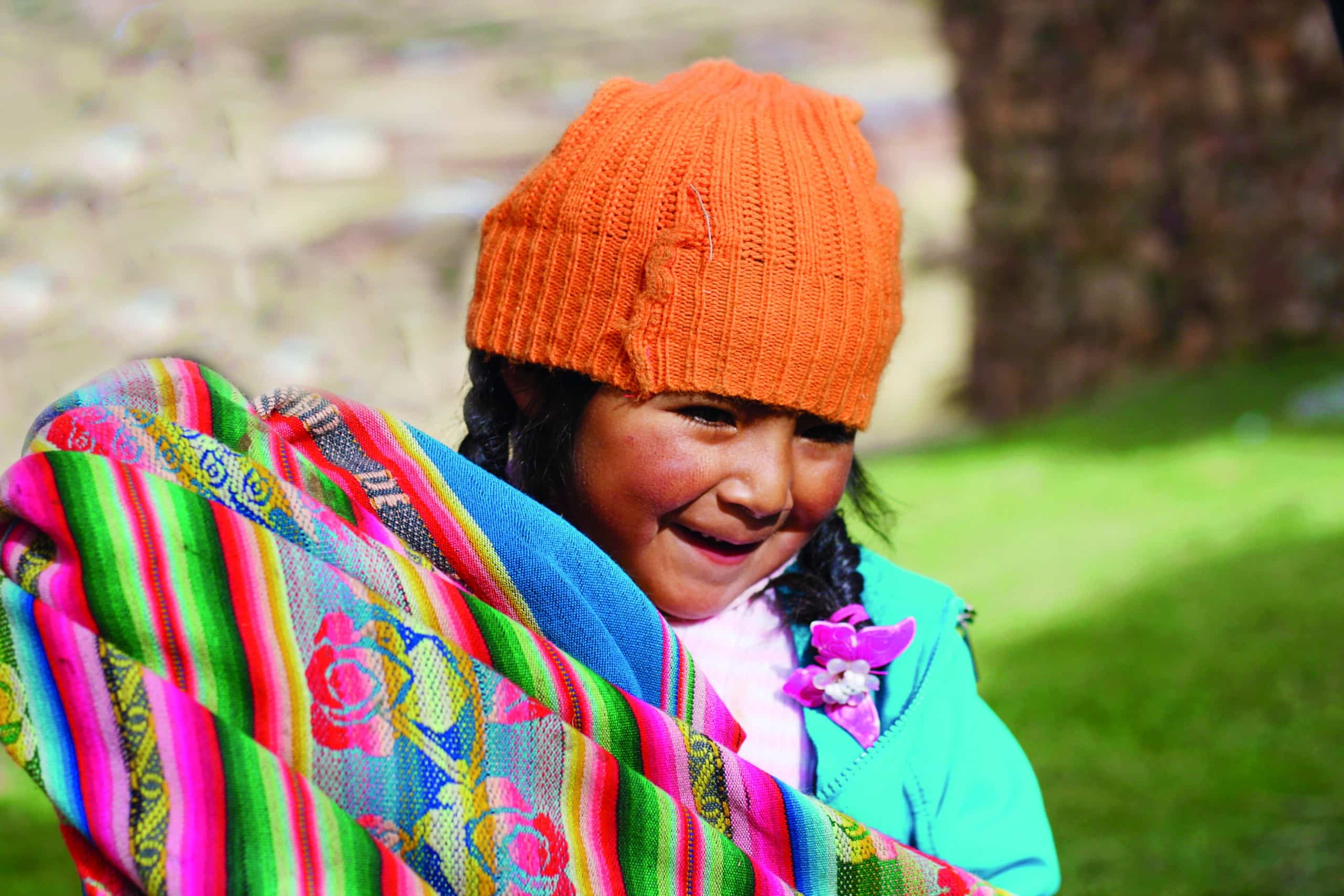 http://Jeune%20fille%20andine%20souriante%20portant%20un%20bonnet%20orange%20et%20un%20textile%20coloré%20au%20Pérou.
