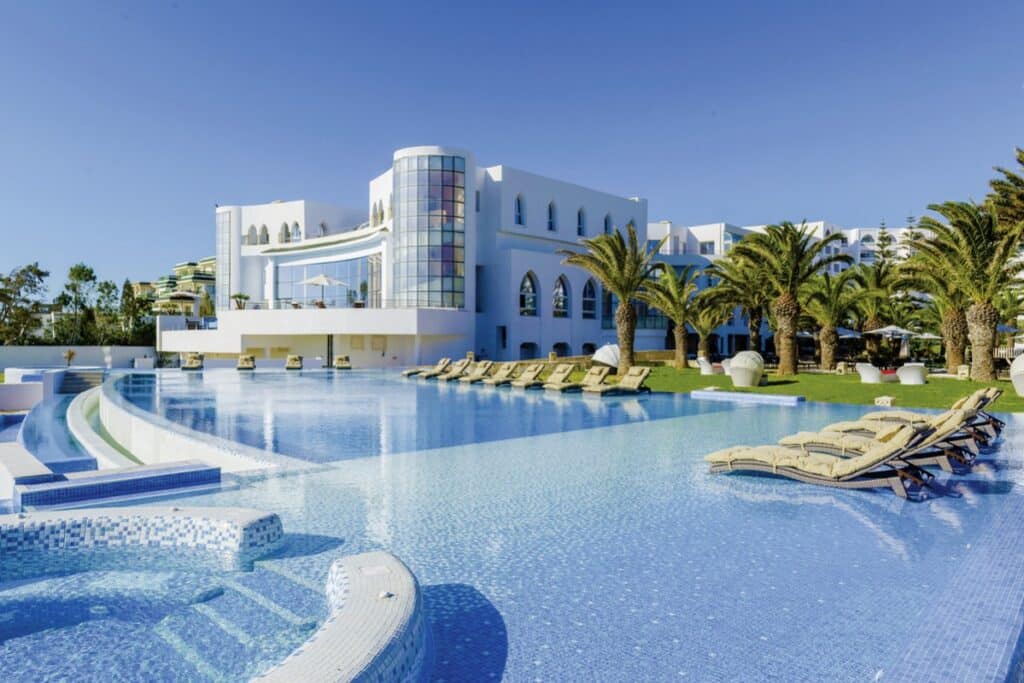 Hôtel moderne en Tunisie avec grande piscine bleue, palmiers et architecture blanche typique.