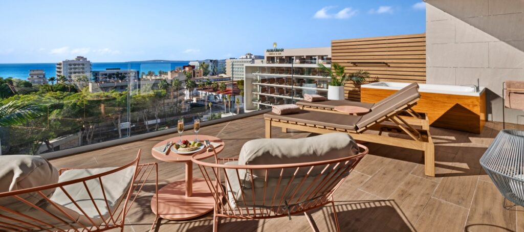 Terrasse d’une suite avec vue sur la mer, transats, table dressée et bain à remous