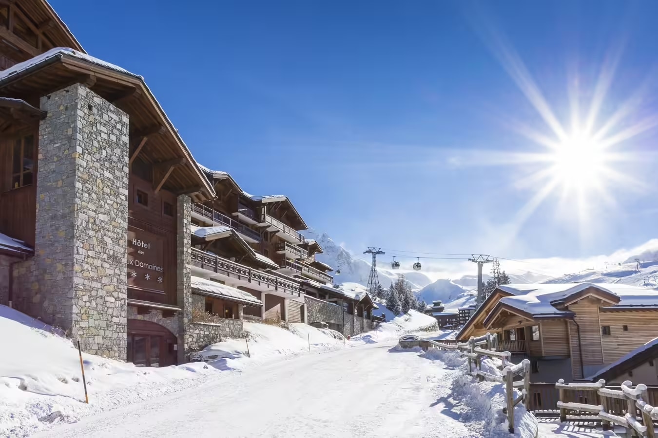 http://Hôtel%20alpin%20en%20bois%20et%20pierre%20sous%20le%20soleil%20avec%20vue%20sur%20les%20pistes%20enneigées%20et%20les%20télécabines