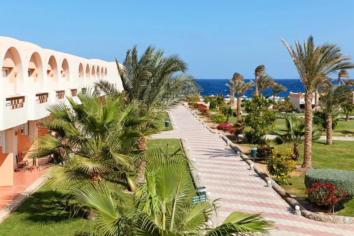 http://Allée%20pavée%20bordée%20de%20palmiers%20et%20jardins%20fleuris%20menant%20à%20la%20plage.