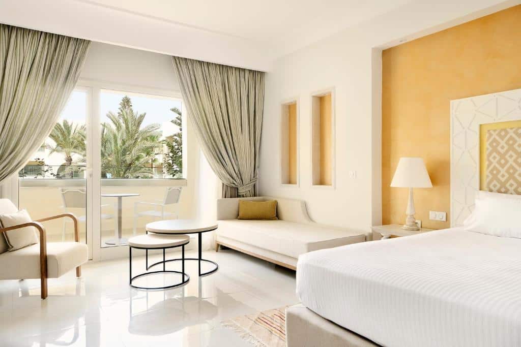 http://Chambre%20d’hôtel%20moderne%20avec%20lit%20double,%20salon%20cosy%20et%20balcon%20donnant%20sur%20les%20palmiers