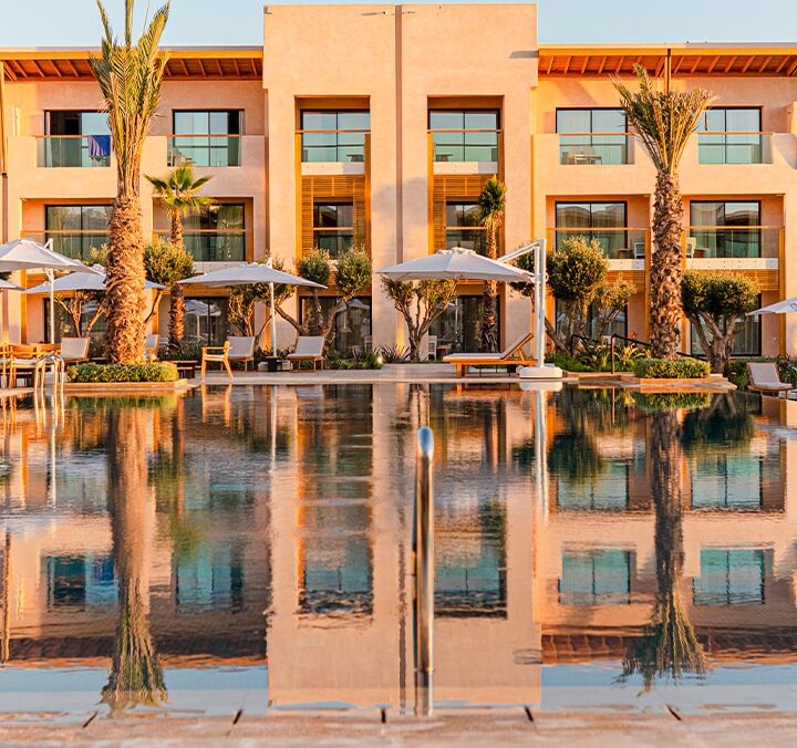 Façade d’hôtel avec piscine reflétant la lumière dorée du coucher du soleil
