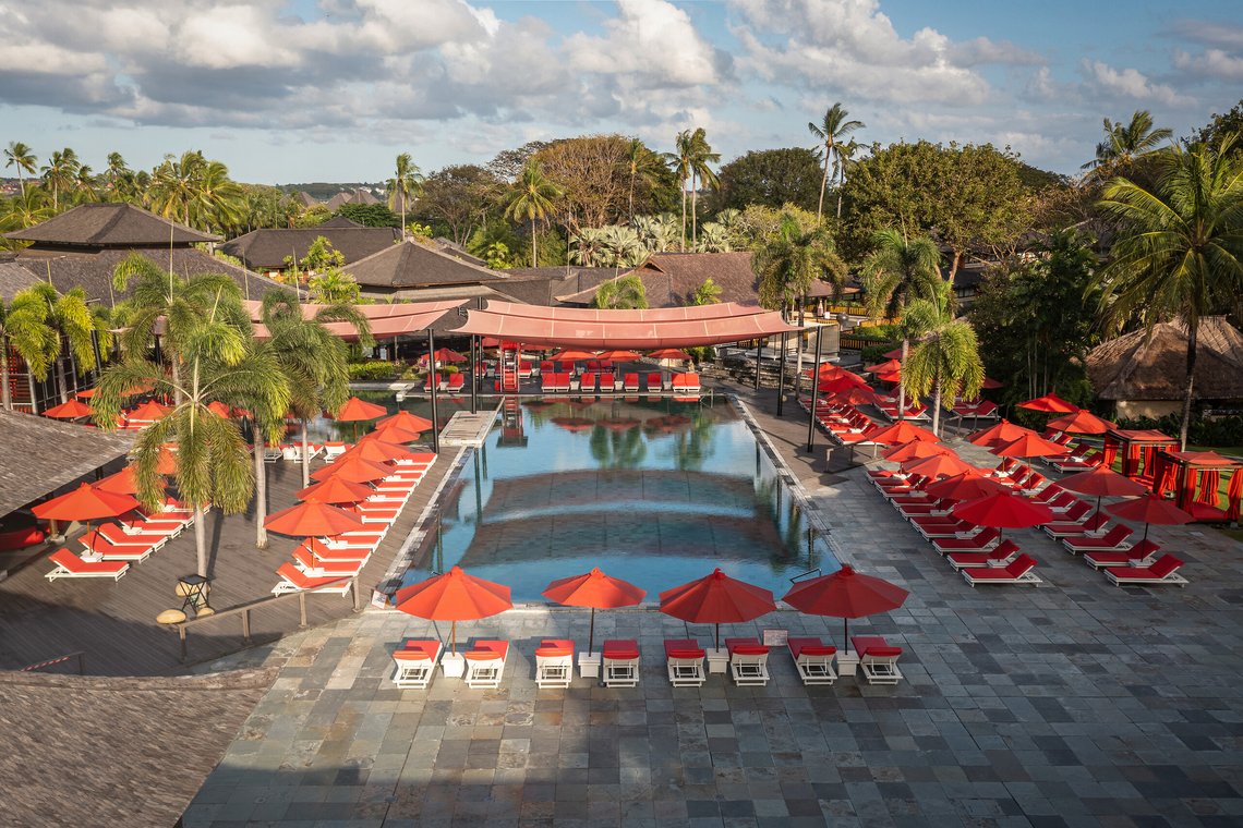 http://Piscine%20élégante%20avec%20parasols%20rouges%20et%20palmiers%20dans%20un%20complexe%20tropical.