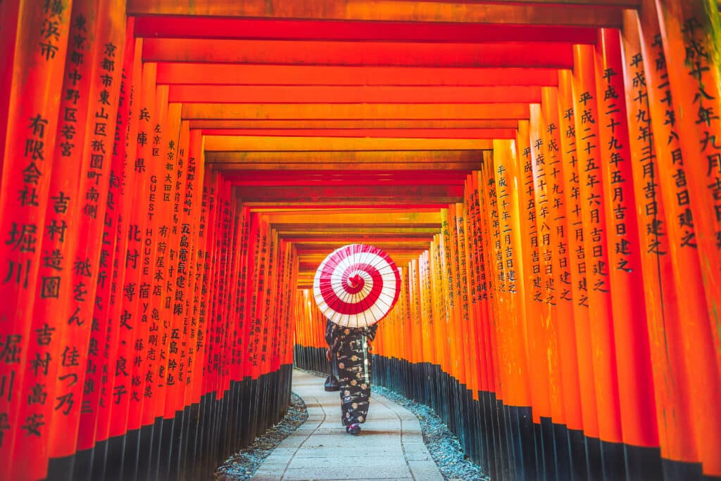 Une femme en kimono sous les milliers de torii rouges du sanctuaire Fushimi Inari à Kyoto.