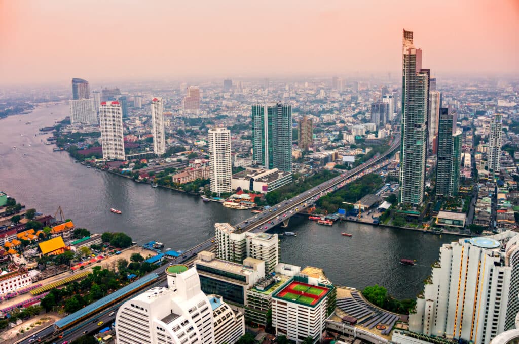 Vue aérienne de Bangkok au crépuscule, avec la rivière Chao Phraya serpentant à travers les gratte-ciel modernes de la ville.