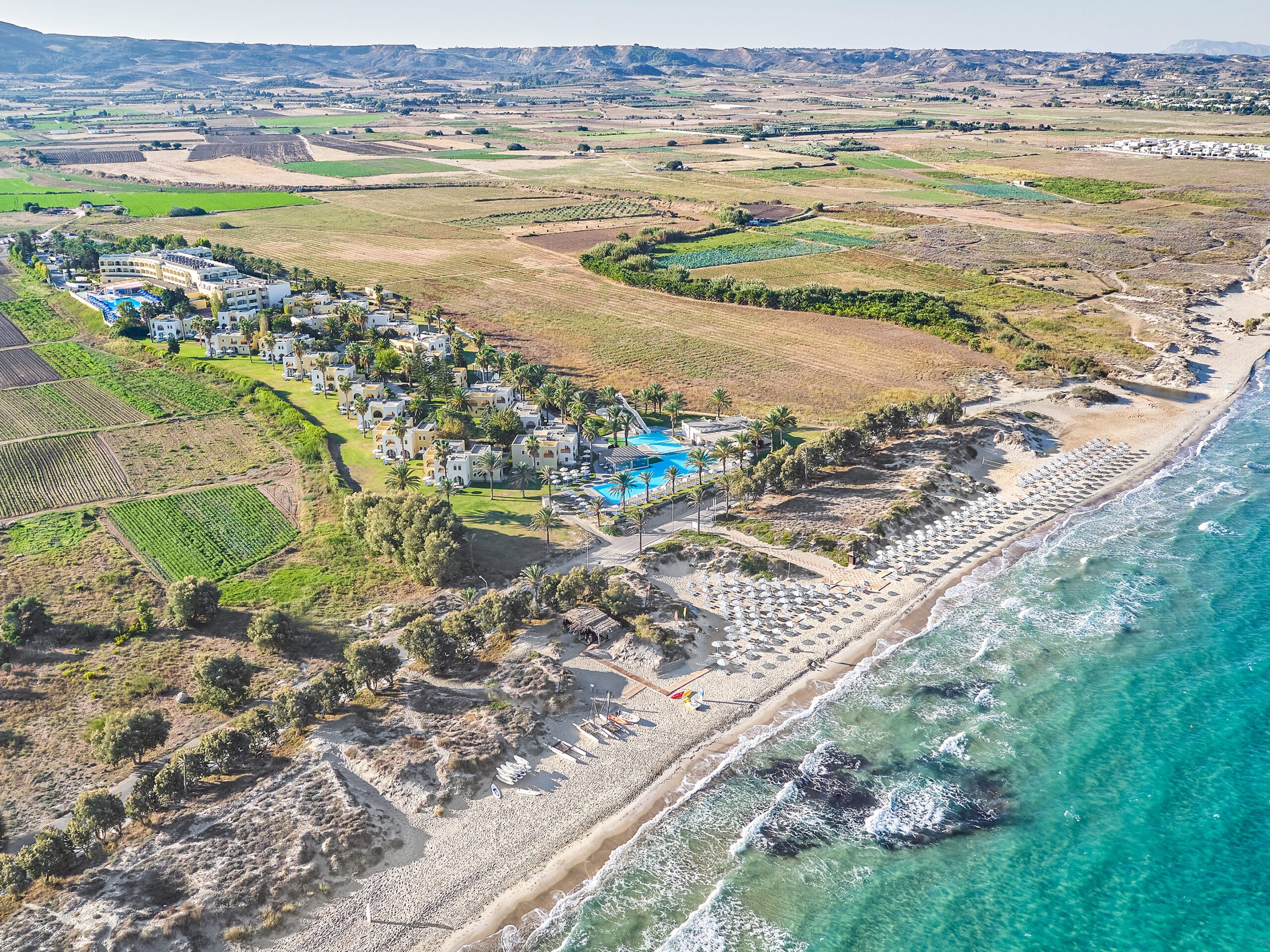 http://Vue%20aérienne%20d’un%20hôtel%20balnéaire%20avec%20plage%20aménagée,%20piscine%20et%20jardins