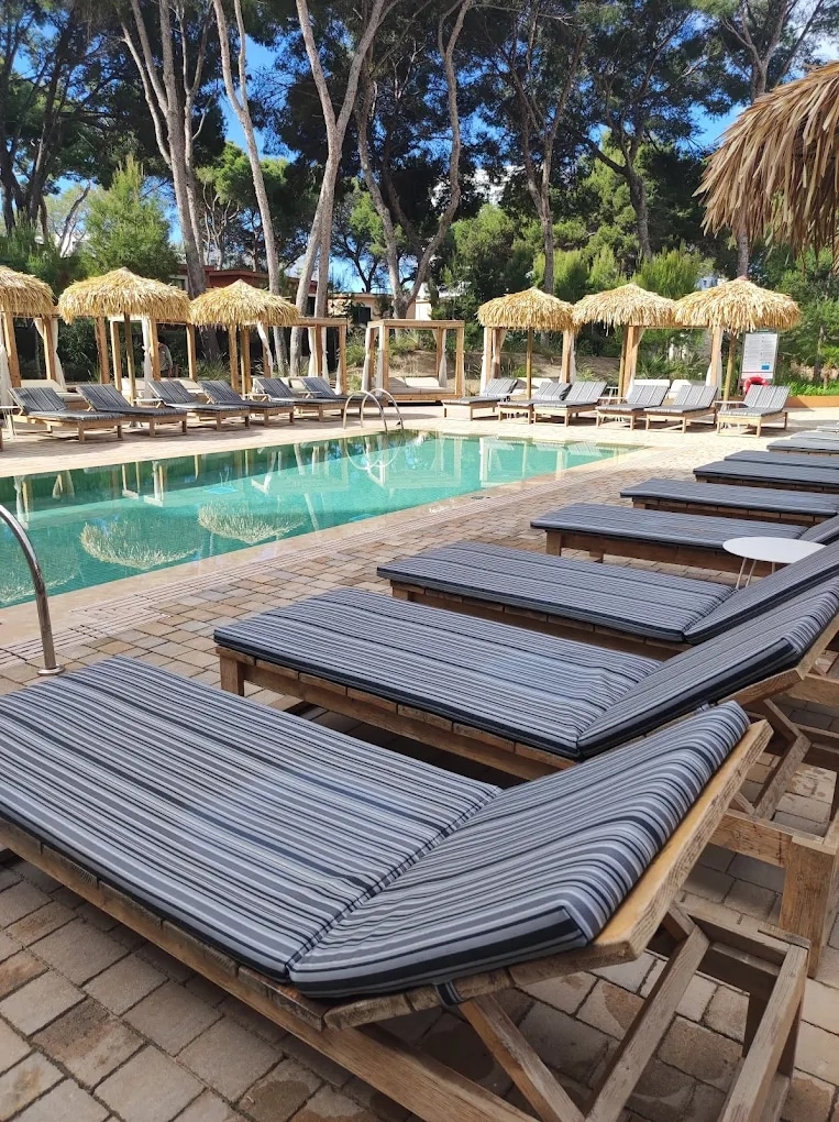 http://Piscine%20extérieure%20avec%20chaises%20longues%20rayées%20et%20parasols%20en%20paille%20dans%20un%20cadre%20arboré.