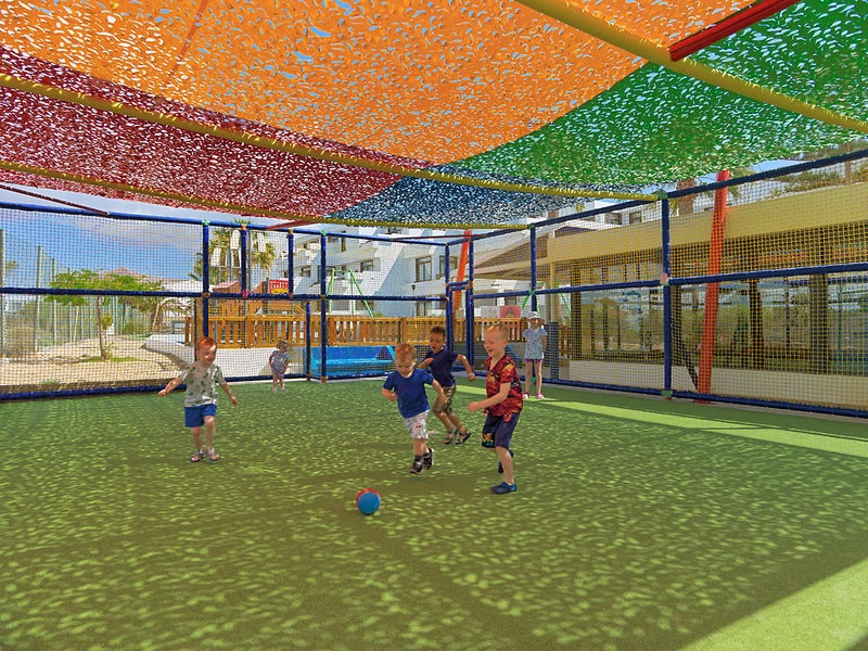 http://Enfants%20jouant%20au%20ballon%20sur%20un%20terrain%20de%20jeu%20extérieur%20couvert%20par%20des%20toiles%20colorées.