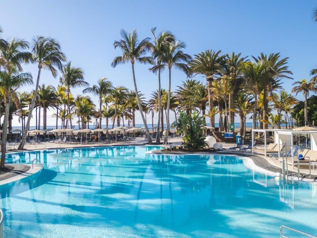 Grande piscine extérieure entourée de palmiers avec vue sur l’océan Atlantique