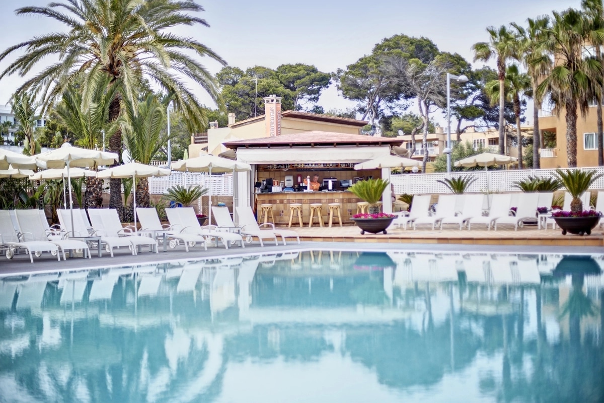 http://Grande%20piscine%20extérieure%20avec%20bar,%20transats%20blancs%20et%20palmiers%20en%20arrière-plan.
