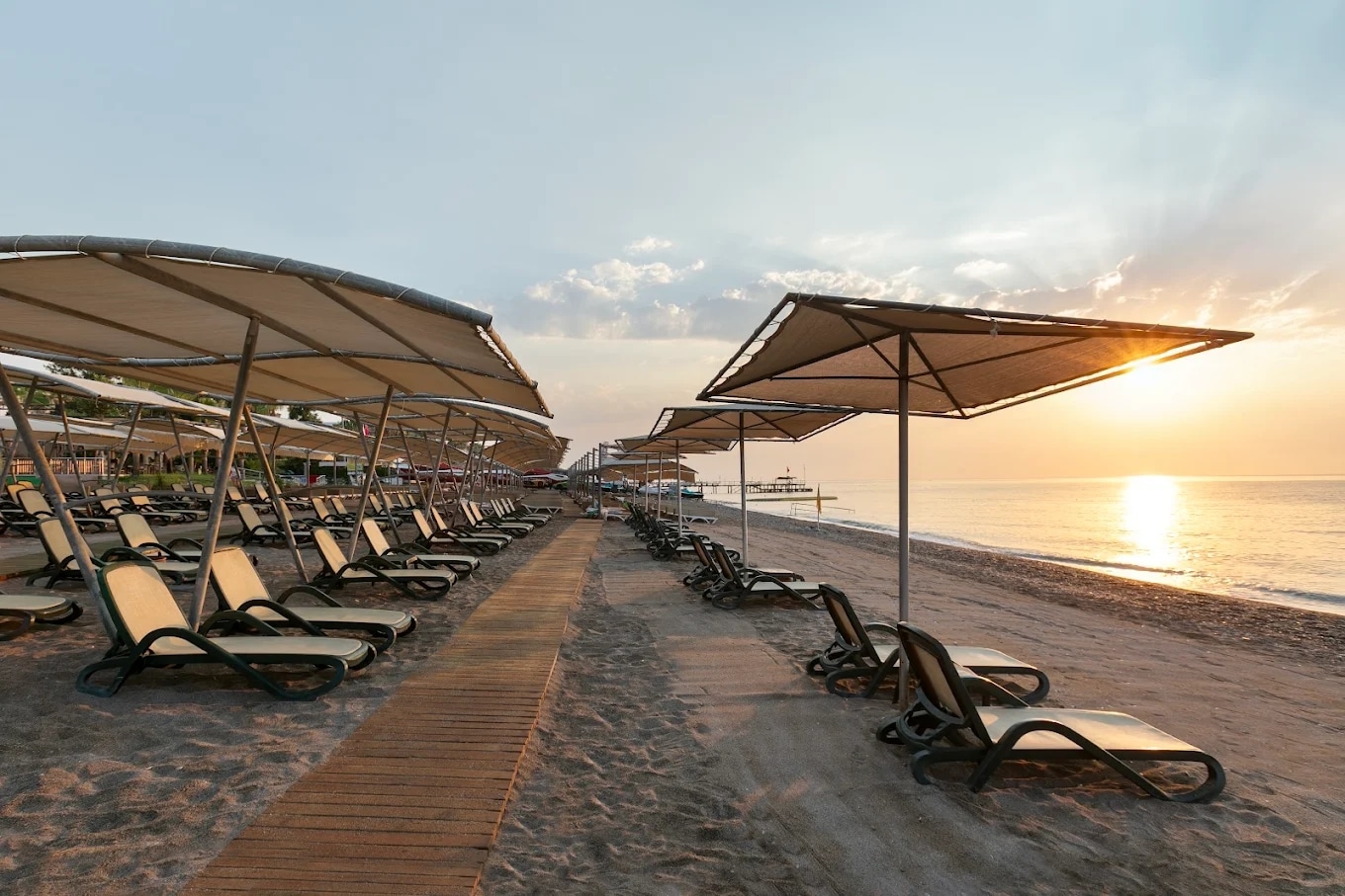 http://Plage%20d’un%20complexe%20hôtelier%20avec%20transats%20vides%20alignés%20sous%20des%20parasols%20au%20lever%20du%20soleil.