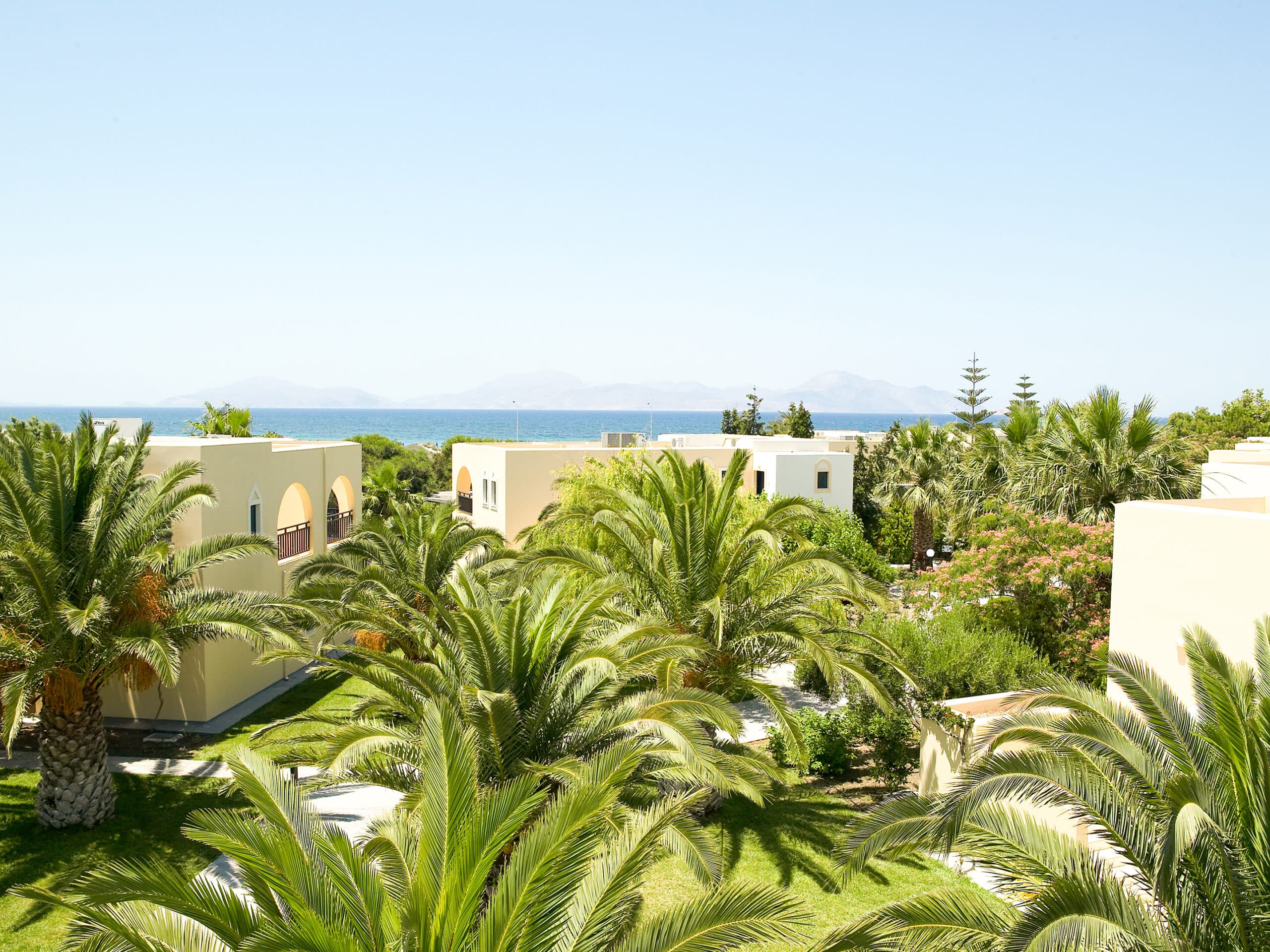 http://Bungalows%20blancs%20entourés%20de%20palmiers%20avec%20vue%20sur%20la%20mer%20et%20montagnes%20au%20loin