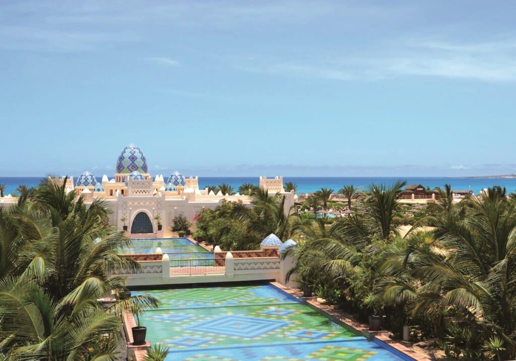 Vue extérieure d'un hôtel de luxe au Cap-Vert, entouré de palmiers avec une architecture inspirée des palais orientaux.