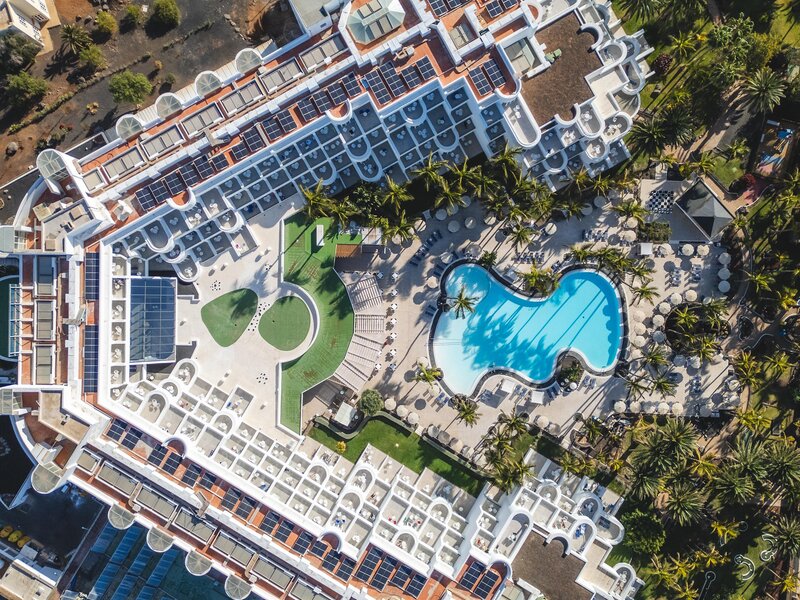 http://Vue%20aérienne%20d’un%20grand%20complexe%20hôtelier%20avec%20piscine%20centrale,%20jardins%20et%20bâtiments%20blancs.