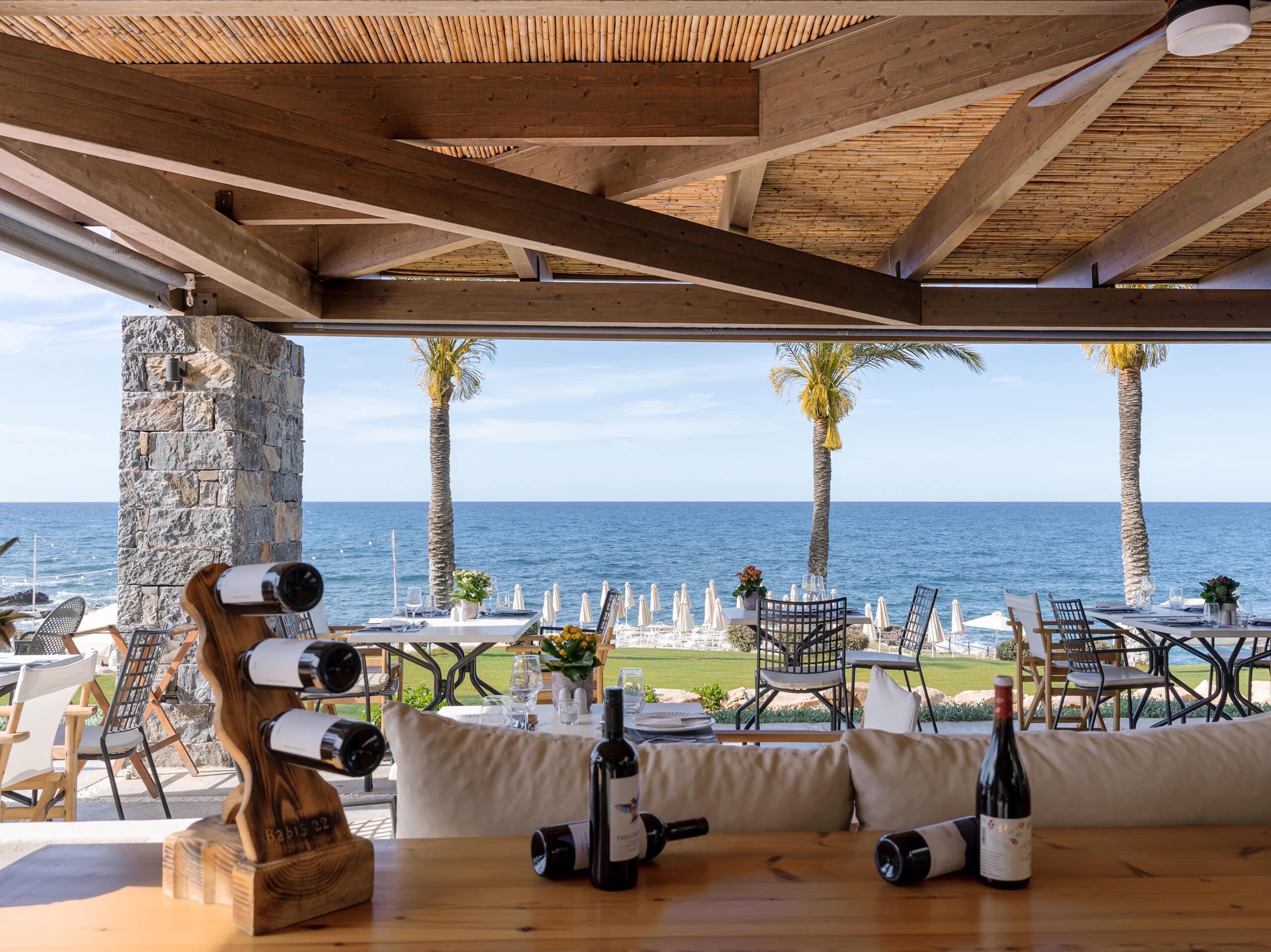 http://Terrasse%20d’un%20restaurant%20en%20bois%20avec%20vue%20sur%20la%20mer%20et%20palmiers%20en%20arrière-plan