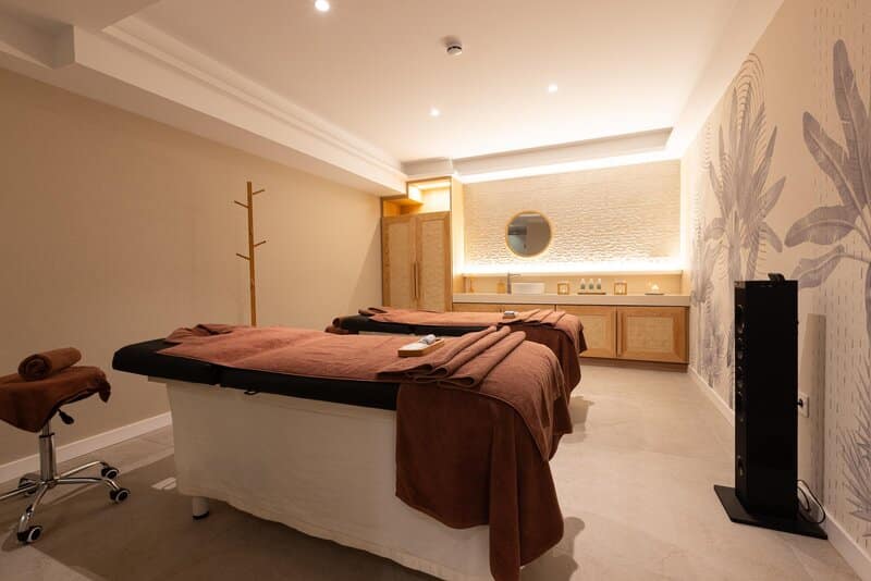 http://Salle%20de%20massage%20pour%20deux%20personnes%20avec%20lits%20de%20soins,%20serviettes%20marron%20et%20lumière%20tamisée.