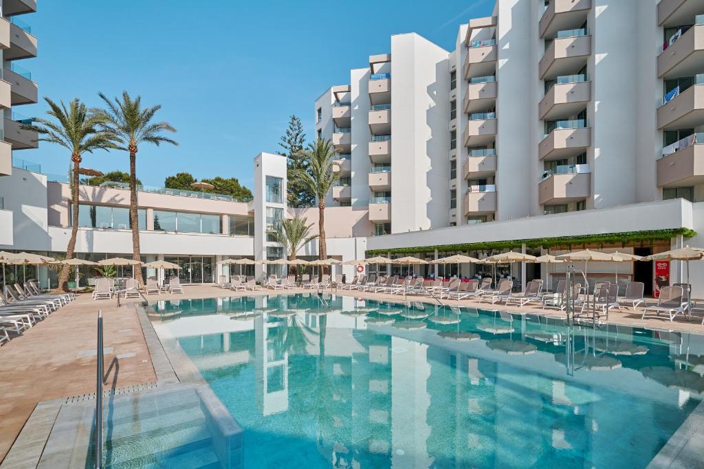 Piscine extérieure avec chaises longues, parasols et palmiers au sein de l’hôtel Bahia Grande