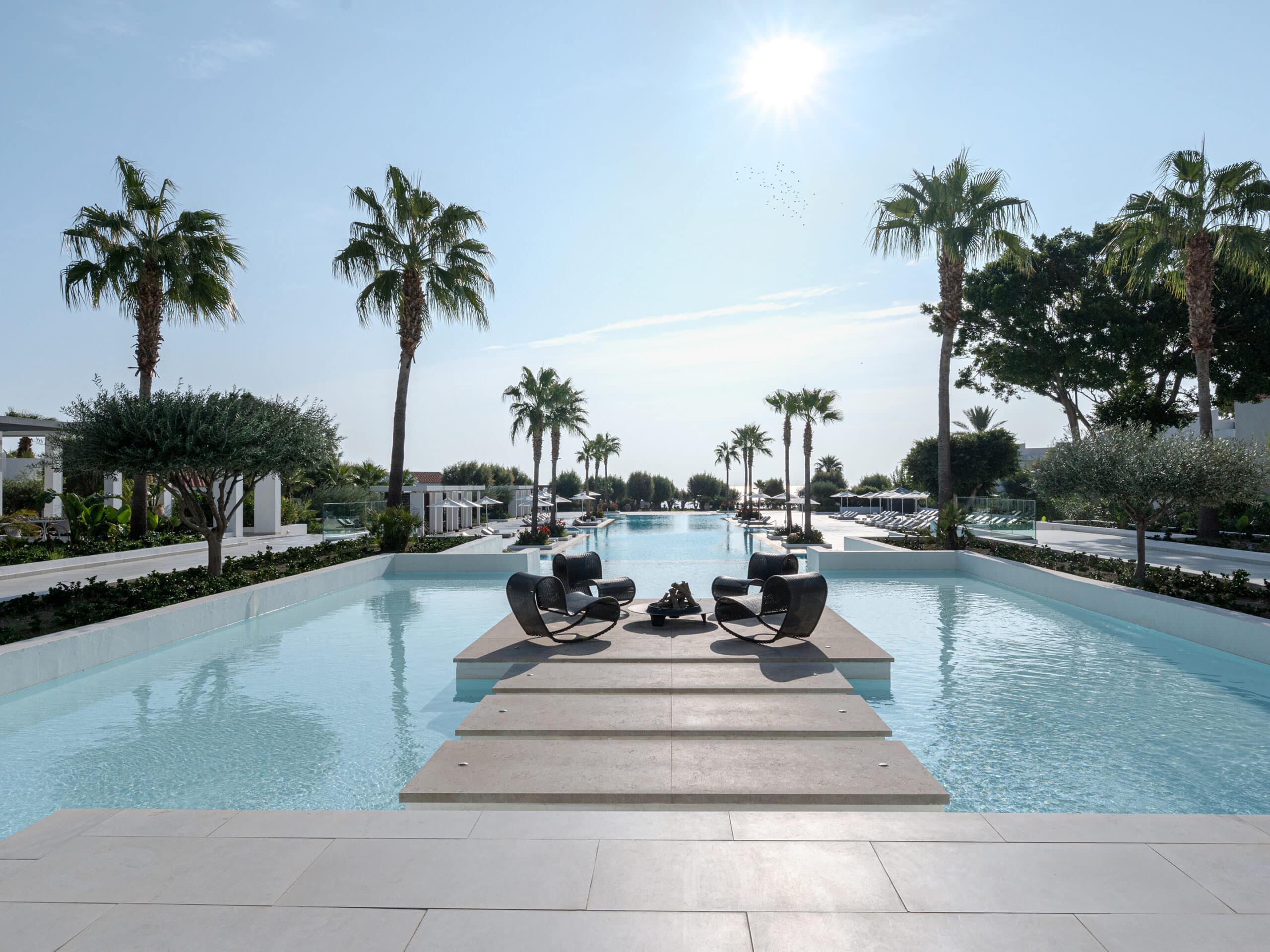 http://Piscine%20contemporaine%20avec%20passerelle,%20palmiers%20et%20fauteuils%20design%20dans%20un%20resort%20de%20luxe.