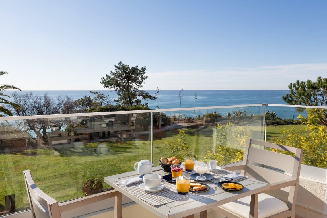 http://Table%20dressée%20pour%20un%20petit-déjeuner%20en%20terrasse%20avec%20vue%20panoramique%20sur%20l'océan%20et%20la%20végétation%20luxuriante%20en%20Algarve,%20Portugal.