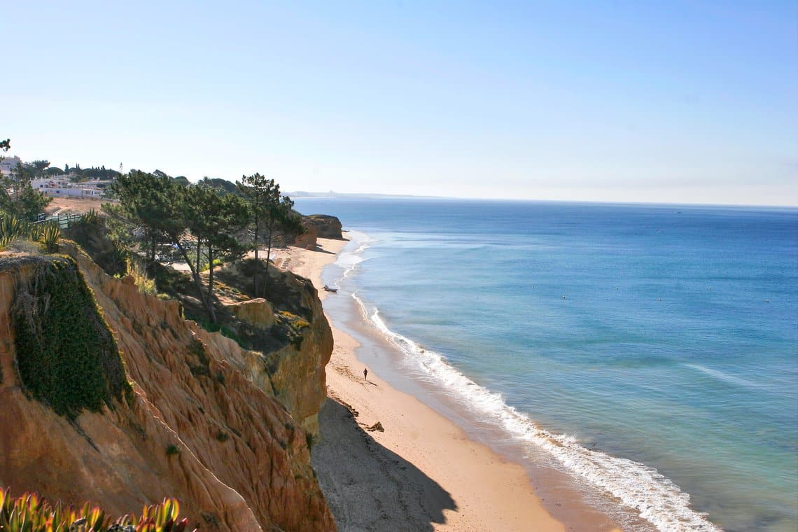 http://Vue%20panoramique%20sur%20une%20plage%20de%20sable%20doré%20bordée%20de%20falaises%20ocres%20et%20de%20pins,%20avec%20l'océan%20Atlantique%20à%20perte%20de%20vue%20en%20Algarve,%20Portugal.