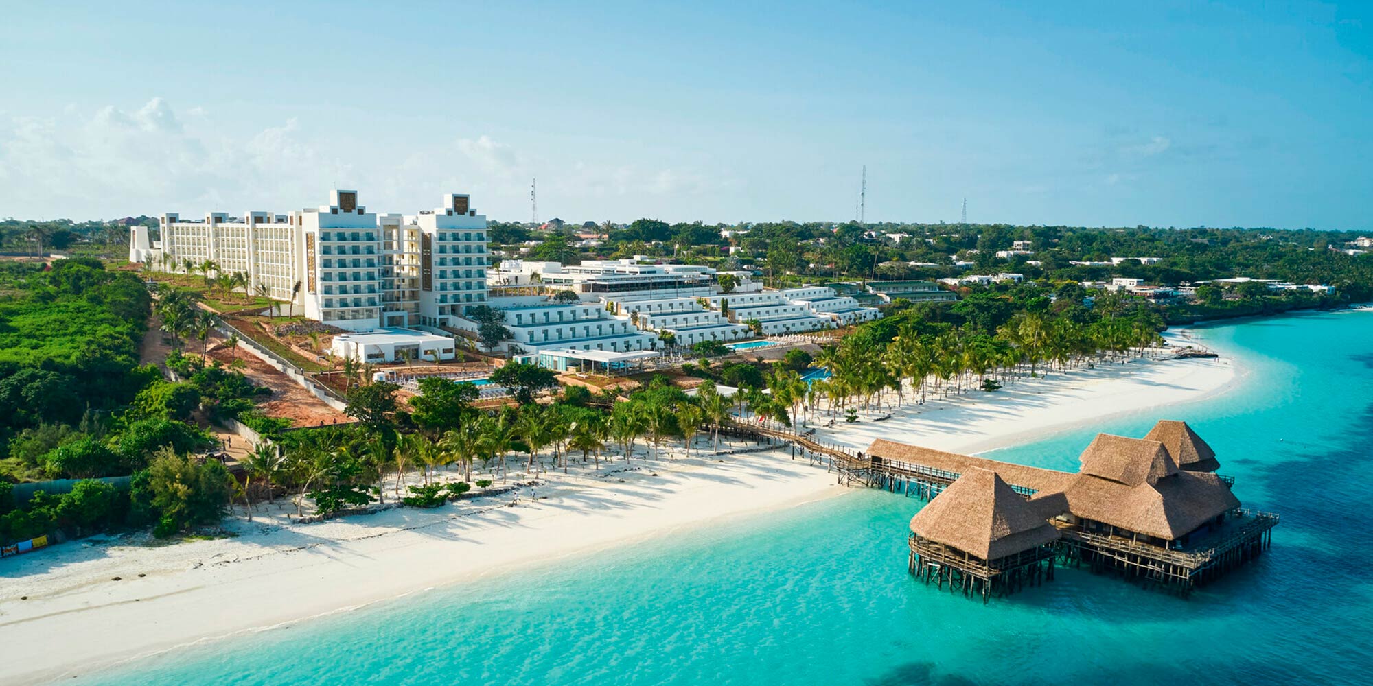 Vue aérienne d’un hôtel de luxe en bord de mer à Zanzibar, avec plage de sable blanc et eau turquoise.