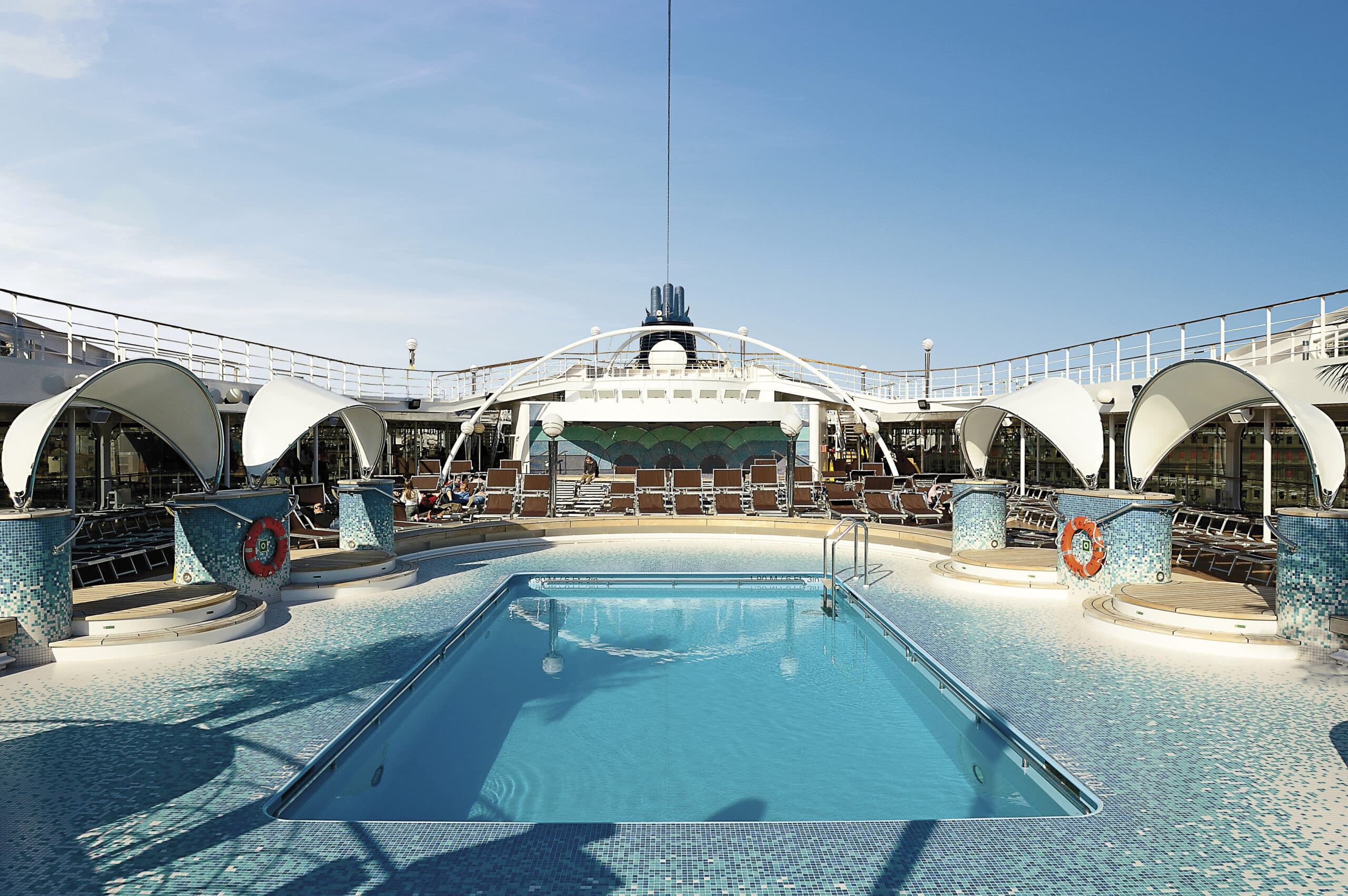 http://Grande%20piscine%20entourée%20de%20transats%20sur%20le%20pont%20supérieur%20d’un%20navire%20de%20croisière%20MSC,%20sous%20un%20ciel%20bleu%20dégagé.