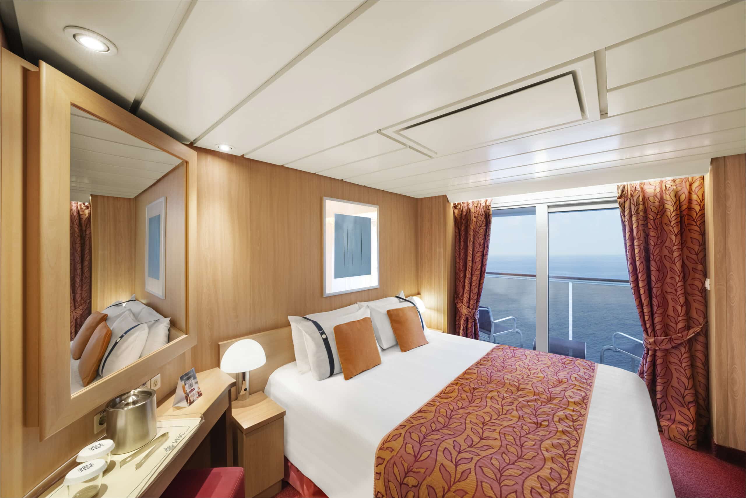 Cabine de croisière avec lit double, mobilier en bois clair, décoration orange et balcon privatif donnant sur la mer.