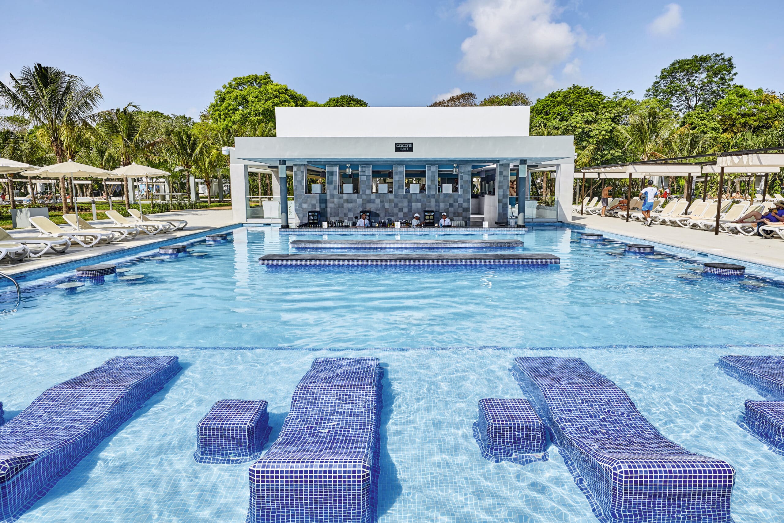 http://Piscine%20avec%20bar%20intégré,%20transats%20aquatiques%20et%20espace%20lounge%20dans%20un%20resort%20tout%20inclus.