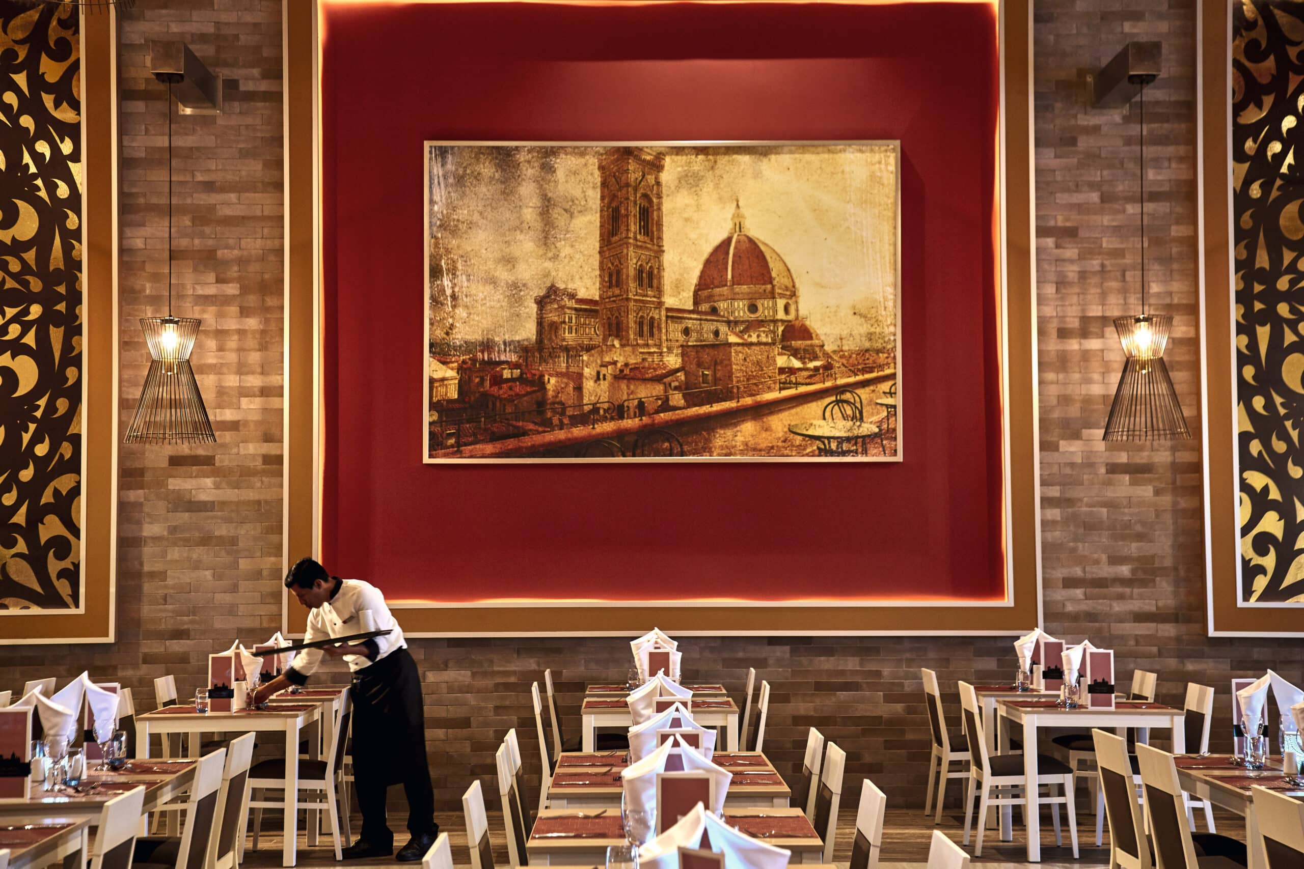 http://Restaurant%20d’hôtel%20avec%20tableau%20de%20Florence,%20tables%20dressées%20et%20serveur%20en%20préparation.