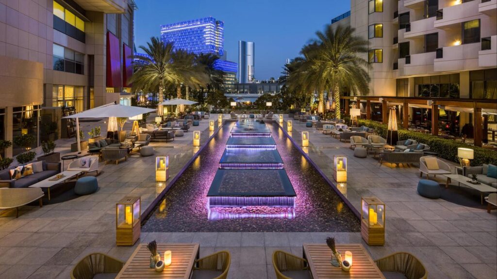 Lounge extérieur d’un hôtel 5 étoiles avec fontaines éclairées et mobilier élégant.