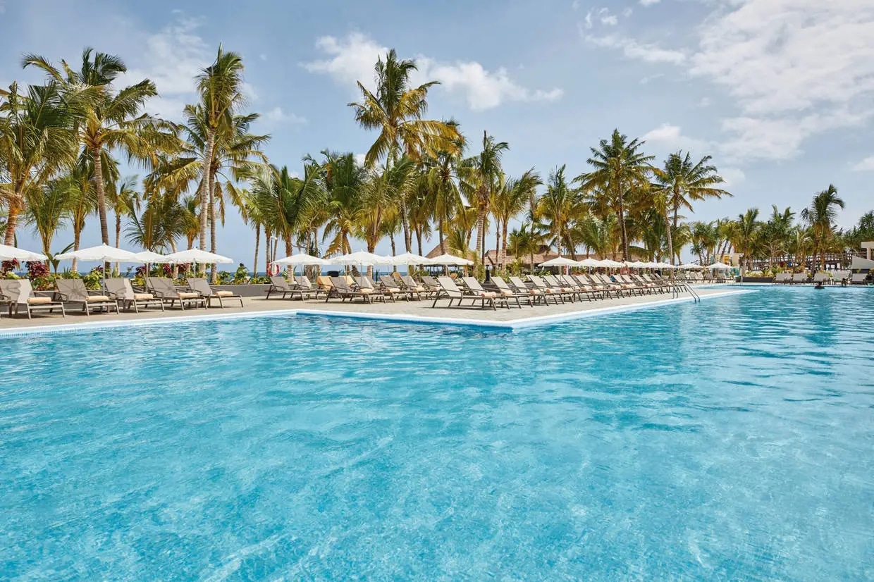 http://Grande%20piscine%20à%20débordement%20avec%20chaises%20longues%20et%20parasols,%20bordée%20de%20palmiers%20tropicaux%20à%20Zanzibar.