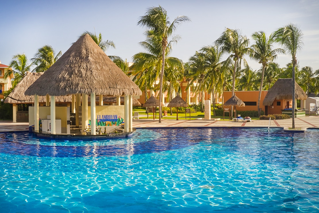 http://Bar%20aquatique%20au%20toit%20de%20chaume,%20intégré%20dans%20une%20piscine%20entourée%20de%20palmiers.