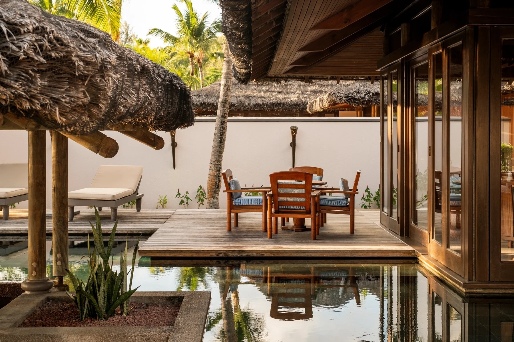 http://Terrasse%20privative%20avec%20mobilier%20en%20bois,%20entourée%20d’un%20bassin%20d’eau%20dans%20un%20resort%20tropical.