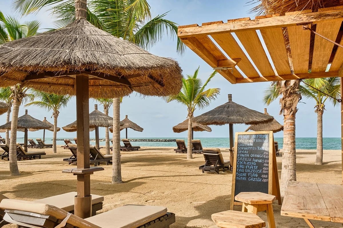 Plage aménagée avec parasols en paille au Grecotel, en Crète, avec vue sur un voilier et mer calme.