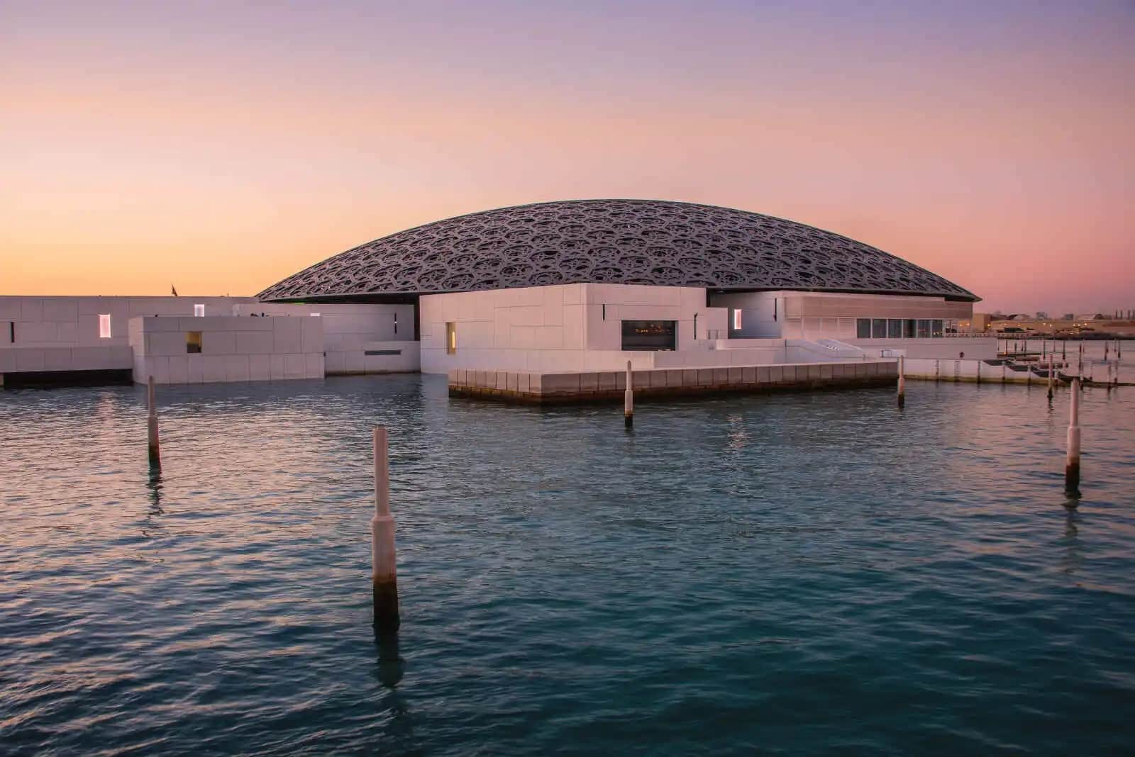 http://Le%20dôme%20du%20Louvre%20Abu%20Dhabi%20illuminé%20au%20coucher%20du%20soleil,%20se%20reflétant%20sur%20les%20eaux%20du%20golfe%20Persique.