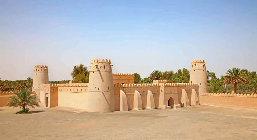 Le fort historique d'Al Jahili en pisé à Al Ain, entouré de palmiers, sous un ciel clair.