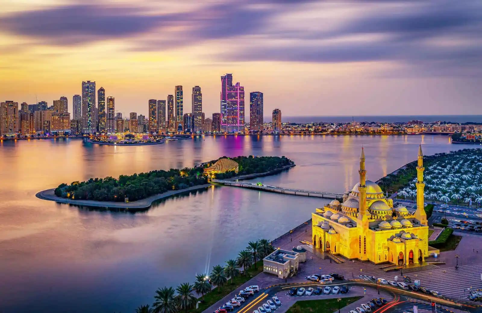 http://Vue%20panoramique%20de%20la%20mosquée%20Al%20Noor%20illuminée%20face%20à%20la%20skyline%20moderne%20de%20Sharjah%20au%20coucher%20du%20soleil,%20Émirats%20arabes%20unis.