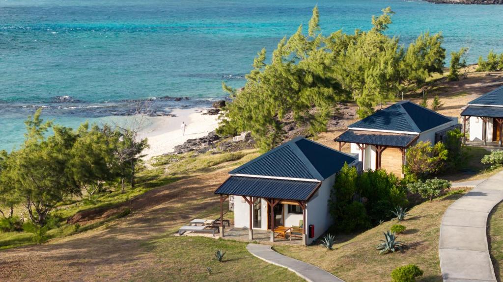 Bungalows en bord de mer entourés de végétation, surplombant une plage de sable fin avec vue sur l’océan.