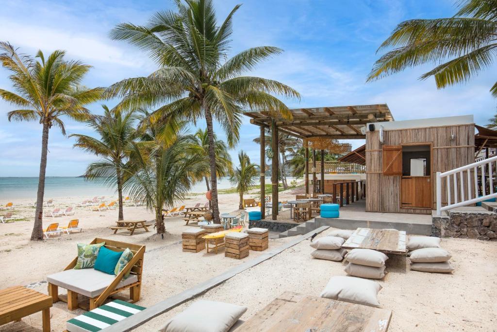 http://Bar%20en%20bois%20sur%20une%20plage%20de%20sable%20blanc,%20entouré%20de%20palmiers%20et%20de%20mobilier%20de%20détente%20en%20plein%20air.