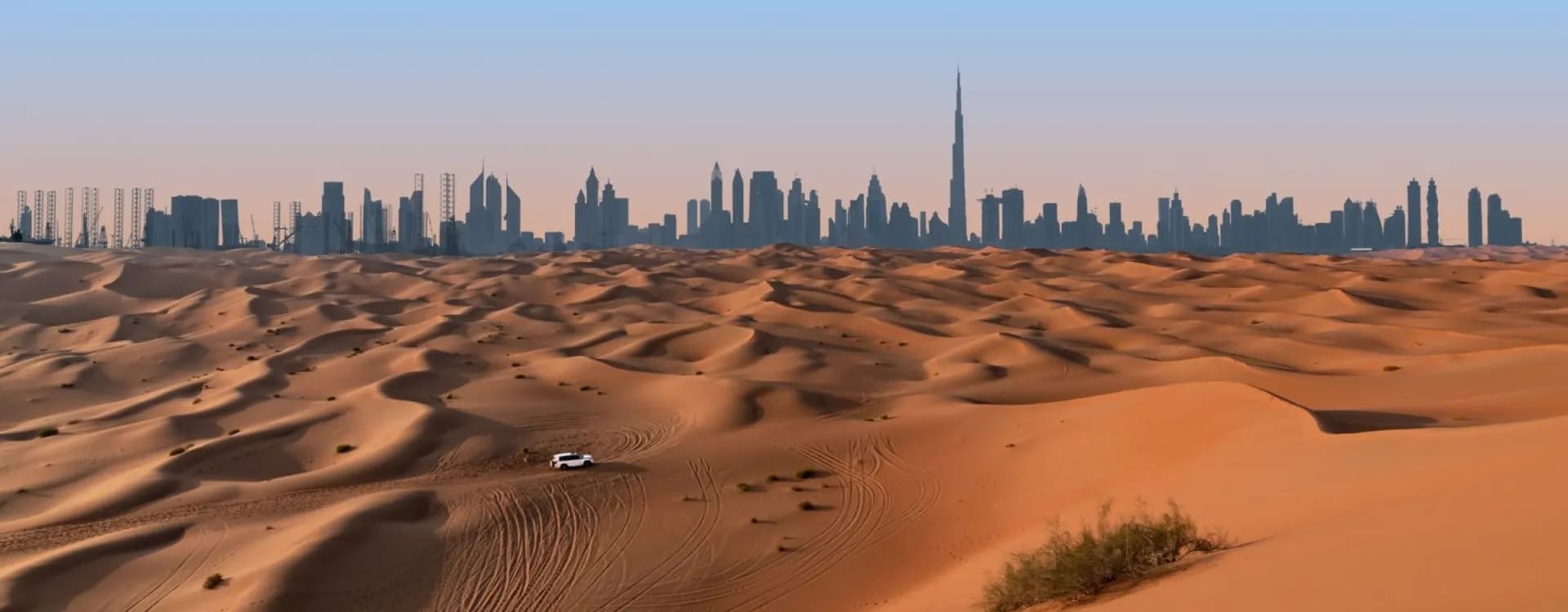 http://Vue%20panoramique%20sur%20les%20dunes%20du%20désert%20avec%20la%20silhouette%20de%20Dubaï%20et%20la%20Burj%20Khalifa%20à%20l’horizon