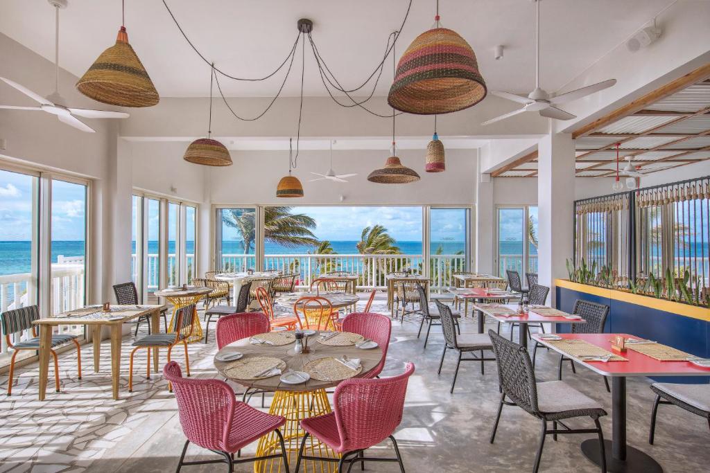 http://Salle%20de%20restaurant%20avec%20baies%20vitrées%20offrant%20une%20vue%20imprenable%20sur%20l’océan,%20mobilier%20coloré%20et%20ambiance%20tropicale.