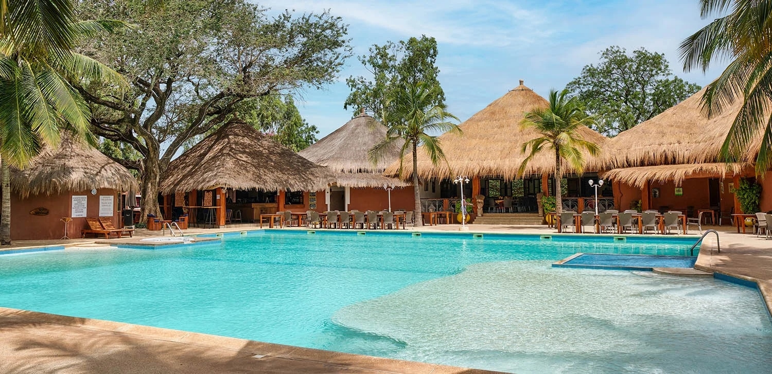http://piscine%20d’un%20hôtel%20au%20Sénégal%20entourée%20de%20palmiers%20et%20de%20bâtiments%20à%20toits%20de%20chaume%20traditionnels