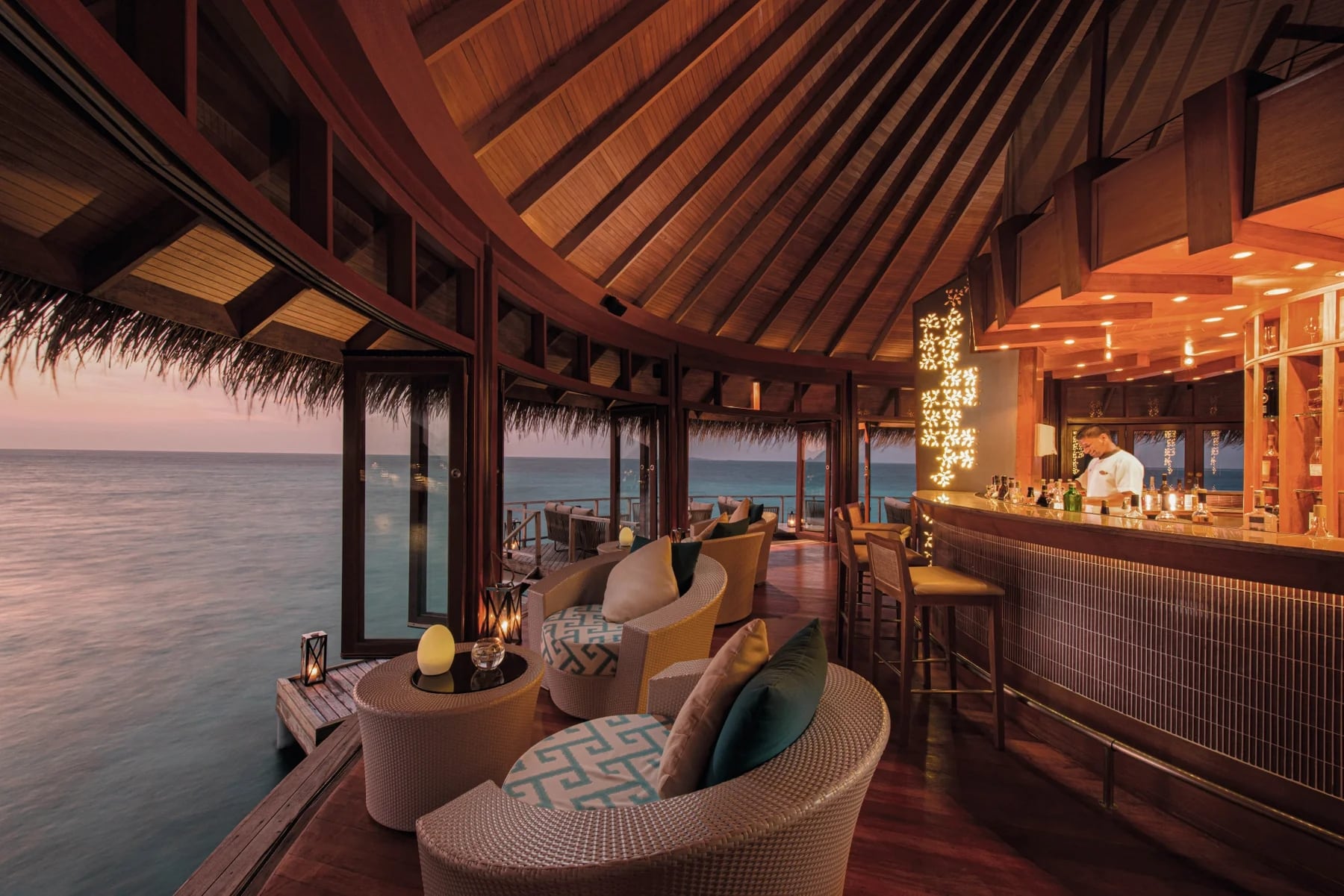 http://Bar%20lounge%20en%20bois%20avec%20mobilier%20raffiné,%20surplombant%20l'océan%20au%20coucher%20du%20soleil.